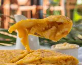 Un tenedor levanta un trozo de tortilla de patatas jugosa, mostrando su interior tierno y dorado.