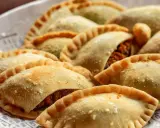 Empanadas doradas y crujientes, algunas con relleno visible de pechuga empanada, espolvoreadas con algo de sal.