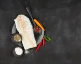 Filete de bacalao fresco listo para preparar a la brasa, con pimienta, sal y chiles.
