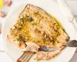 Deliciosa trucha al ajillo servida en un plato, con ajos y aceite de oliva alrededor.
