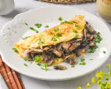 Tortilla de champiñones, dorada y esponjosa, rellena de sabrosos champiñones salteados y espolvoreada con perejil fresco.
