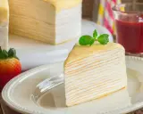 Una porción de tarta de crepes, decorada con menta, junto a fresas y un vaso de batido de fresa.