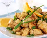 Sabroso pollo a la naranja, trozos jugosos con rodajas de naranja fresca y cebolleta picada, servido en un plato blanco.