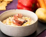 Deliciosa ensaladilla de pulpo cremosa, servida en cuenco, con patata, pimiento y zanahoria de fondo.