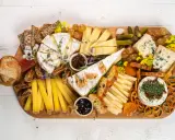 Una tabla de quesos sencilla con variedad de quesos, pan, frutas secas, uvas, pepinillos y mermelada.