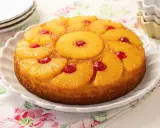 Tarta de piña dorada y jugosa, decorada con rodajas de piña caramelizada y cerezas rojas.