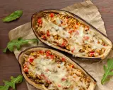 Dos mitades de berenjenas rellenas con cuscús, pimientos y queso derretido, cocinadas en airfryer.