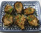 Seis mitades de alcachofas a la plancha, doradas y espolvoreadas con perejil fresco, servidas en un plato decorado.