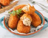Croquetas de atún doradas y crujientes, servidas en un cuenco azul. Una está partida, mostrando su cremoso interior.