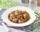 Plato de tierna carne de cerdo en salsa, servido en un cuenco blanco con un tenedor y decoración floral.
