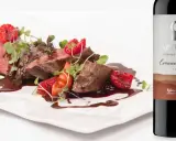 Filete de ternera con fresas y frambuesas, bañado en salsa, junto a una botella de vino Vetusta de la **Ribera del Duero**.