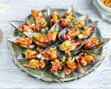 Mejillones a la vinagreta servidos en una bandeja de cristal, adornados con una colorida mezcla de pimientos y cebolla.