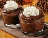 Dos copas de cremosas natillas de chocolate con nata montada, decoradas con piñas y hojas de otoño.
