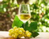 Copa de vino blanco con uvas verdes y hojas de parra.