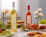 Dos botellas de vino, blanco y rosado, acompañadas de frutas, frutos secos y pequeños bocadillos. Un festín de tinta del país.