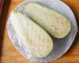 Dos mitades de berenjena cortadas en cubos y cubiertas con plástico, listas para cocinar berenjenas al microondas.