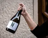 Mano sujeta botella de txakoli tinto Nekazari, con etiqueta blanca y letra "N" verde.