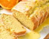 Un delicioso bizcocho de naranja, cubierto con glaseado y ralladura, con dos rebanadas cortadas.