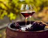 Dos copas de vino tinto y racimos de uvas sobre un barril de madera, evocando las mejores añadas de Ribera del Duero.