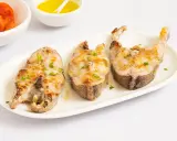 Tres rodajas de mero a la plancha, doradas y con perejil picado, servidas en plato blanco.