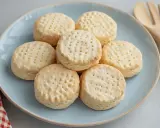 Un plato azul con galletas de maíz horneadas, cada una con pequeños agujeros en la parte superior. Un paño a cuadros rojos y blancos y un utensilio de madera están cerca.