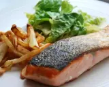 Un jugoso salmón a la plancha con piel crujiente, acompañado de papas fritas doradas y una fresca ensalada verde.