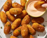 Croquetas de patata doradas y crujientes, espolvoreadas con perejil y sal, listas para ser mojadas en una cremosa salsa rosa.