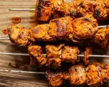 Cuatro brochetas de pinchos morunos auténticos, jugosos y dorados, sobre una tabla de madera.