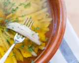 Boquerones en vinagre, la receta de la abuela, listos para disfrutar. Un tenedor recoge un boquerón marinado en aceite y vinagre, espolvoreado con perejil.