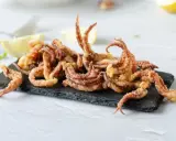 Crujientes rejos fritos servidos sobre pizarra negra, acompañados de gajos de limón.