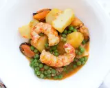 Patatas a la marinera con gambas, mejillones y guisantes en una salsa sabrosa.