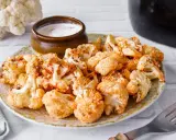 Coliflor airfryer dorada y crujiente servida en un plato con un tazón de salsa.