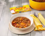 Un tazón de lentejas con zanahoria y pimiento rojo, listo para servir. La caja de Avecrem Pollo de corral, clave en esta lentejas receta de la abuela, descansa al lado.