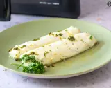 Dos filetes de merluza jugosos, recién salidos de la airfryer, con hierbas frescas y aceite de oliva.