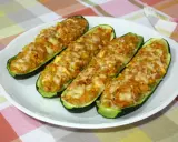 Cuatro calabacines rellenos de atún, gratinados con queso, servidos en un plato blanco sobre un mantel a cuadros.