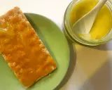 Galleta con mermelada de aceite de oliva, servida en plato verde junto a un tarro con la mermelada y una cuchara.