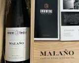Caja de vino "Malaño" con etiqueta "Vino Solidario" y logos de INNWINE y feder. Incluye folleto informativo.