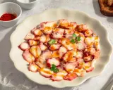 Delicioso carpaccio de pulpo, finas láminas con pimentón y perejil, servido en plato blanco.