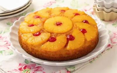 Tarta de piña dorada y jugosa, decorada con rodajas de piña caramelizada y cerezas rojas.