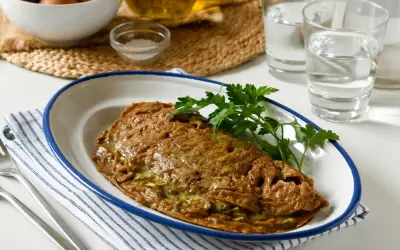 Tortilla de alcachofas dorada y jugosa, servida en plato blanco con borde azul. Decorada con perejil fresco.