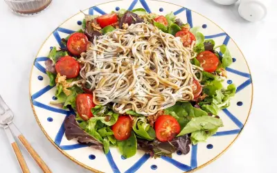 Deliciosa ensalada de gulas con tomates cherry y hojas verdes, servida en un plato decorado.