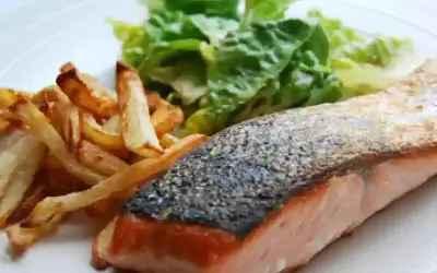 Un jugoso salmón a la plancha con piel crujiente, acompañado de papas fritas doradas y una fresca ensalada verde.