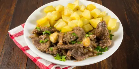 Plato de higaditos de pollo en salsa con patatas fritas en cubos, decorado con perejil fresco.