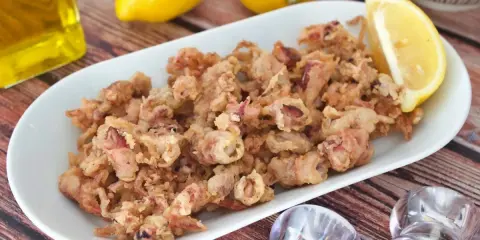 Crujientes puntillas de calamar fritas en un plato blanco, acompañadas de limón y aceite de oliva.