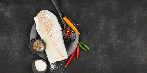 Filete de bacalao fresco listo para preparar a la brasa, con pimienta, sal y chiles.