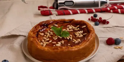 Bizcocho de avena casero, glaseado y decorado con piñones y menta. Frutos rojos y batidora al fondo.