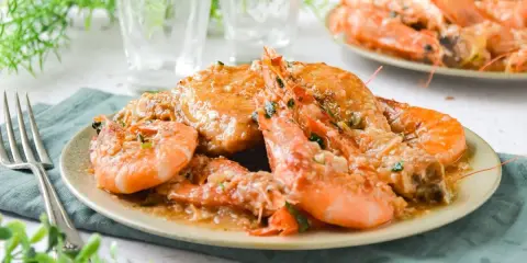 Plato de pollo con gambas en salsa, decorado con perejil picado. Se ve delicioso y listo para disfrutar.