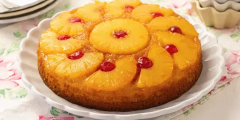 Tarta de piña dorada y jugosa, decorada con rodajas de piña caramelizada y cerezas rojas.