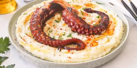 Delicioso pulpo a la brasa sobre puré de patatas cremoso, espolvoreado con pimentón y perejil.