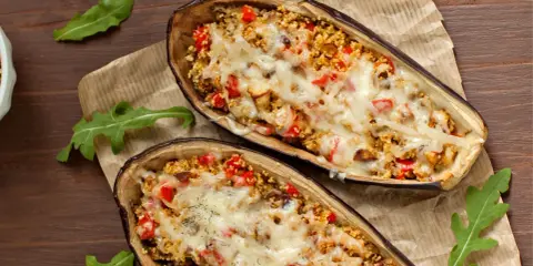 Dos mitades de berenjenas rellenas con cuscús, pimientos y queso derretido, cocinadas en airfryer.